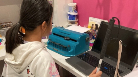 Una niña ciega prepara sus tareas de clase delante de una maquina Perkins y un ordenador.